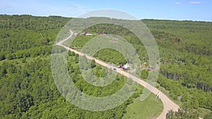 Aerial view of car moving on the countryside road near the cottages surrounded by meadows and forest with coniferous and