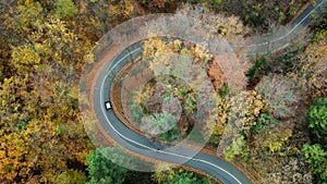 Aerial view of car passing curvy road in forest. Autumn high in mountains