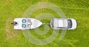 Aerial view car with a white fishing motor boat at the trailer at the green grass. Top aerial view car with fishing boat on traile