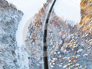 Aerial view of a car on winter road in the forest. Winter landscape countryside. Aerial photography of snowy forest with a car on