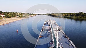 Aerial view of cargo commercial ship sailing down the river surrounded by green forest on a summer sunny day. Footage