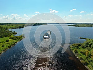 Aerial view the cargo ship floats down the river surrounded by forest. Beautiful panoramic landscape from the height