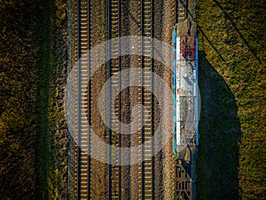 Aerial view of cargo train, a double-track railway in countryside. Railroad with green grass and trees with long shadows, top view