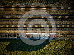 Aerial view of cargo train, a double-track railway in countryside. Railroad with green grass and trees with long shadows, top view