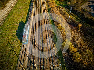 Aerial view of cargo train, a double-track railway in countryside. Railroad with green grass and trees with long shadows, top view