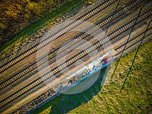 Aerial view of cargo train, a double-track railway in countryside. Railroad with green grass and trees with long shadows, top view