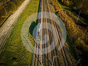 Aerial view of cargo train, a double-track railway in countryside. Railroad with green grass and trees with long shadows, top view