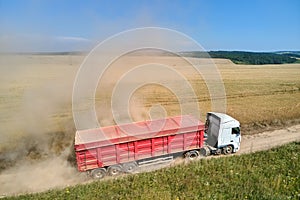 Aerial view of cargo truck driving on dirt road between agricultural wheat fields making lot of dust. Transportation of