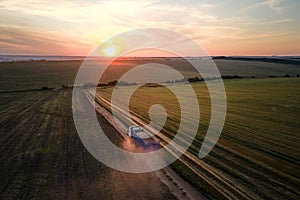 Aerial view of cargo truck driving on dirt road between agricultural wheat fields making lot of dust. Transportation of