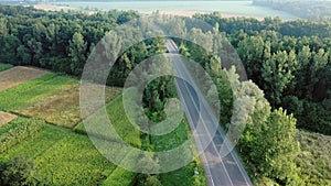 Aerial view of cars driving along the empty roadriding along trees and fields on sunny morning.Travelling, car rental