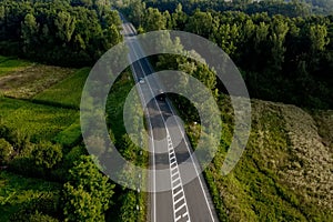 Aerial view of cars driving along the empty roadriding along trees and fields on sunny morning.Travelling, car rental