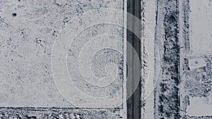 Aerial view of cars driving along a rural road surrounded by fields in winter