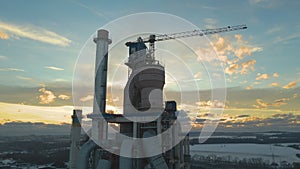 Aerial view of cement plant with high factory structure and tower crane at industrial production area.