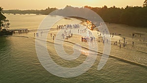 Aerial view of children in white uniforms playing on beach at sunset. Pupils enjoy coastal waves, warm light reflecting