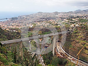 an aerial view of the city of funchal in madeira with a bridge carrying the vr1 motorway crossing the valley and construction work