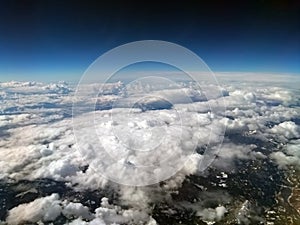 Aerial view of cloud covered mountain landscape with snow visible on green hills with dark sky with the curvature of the earth