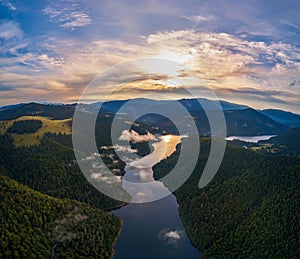 Aerial view clouds over the forest and lake at sunrise. View from drone. Aerial top view cloudscape. Transylvania, Romania