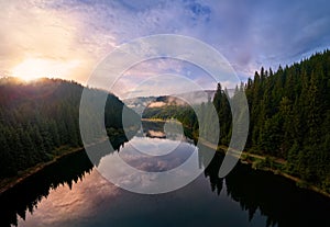 Aerial view clouds over the forest and lake at sunrise. View from drone. Aerial top view cloudscape. Transylvania, Romania