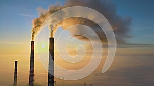 Aerial view of coal power plant high pipes with black smoke moving up polluting atmosphere at sunrise.