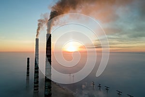 Aerial view of coal power plant high pipes with black smoke moving up polluting atmosphere at sunset