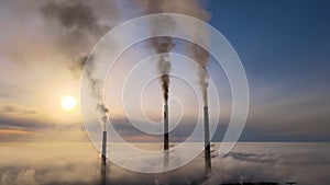 Aerial view of coal power plant high pipes with black smoke moving up polluting atmosphere at sunset