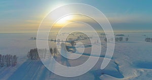 Aerial view of cold winter landscape arctic field, trees covered with frost snow, ice river and sun rays over horizon