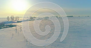 Aerial view of cold winter landscape arctic field, trees covered with frost snow, ice river and sun rays over horizon