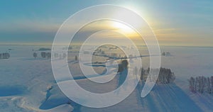 Aerial view of cold winter landscape arctic field, trees covered with frost snow, ice river and sun rays over horizon