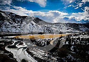 Aerial view of the Colorado River in winter, surrounded by snow-capped mountains and evergreen trees