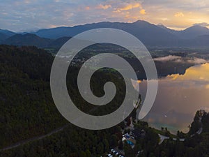 Aerial view of the colorful forest and Lake Bled with a small island with a church. Sunrise in Slovenia in the fall. Castle, aeria