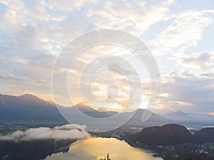 Aerial view of the colorful forest and Lake Bled with a small island with a church. Sunrise in Slovenia in the fall. Castle, aeria