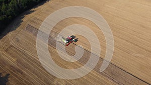 Aerial view of combine harvester and tractor harvesting wheat from field. The camera slowly goes down