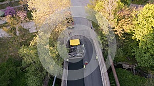 Aerial view of the construction of a new road as asphalt pavers, rollers, machinery, and workers come together to build