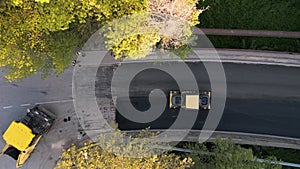 Aerial view of the construction of a new road as asphalt pavers, rollers, machinery, and workers come together to build