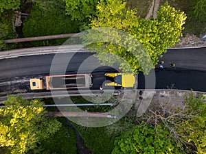 Aerial view of the construction of a new road as asphalt pavers, rollers, machinery, and workers come together to build