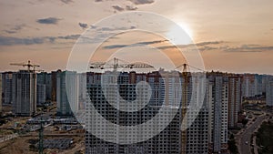 Aerial view of construction site of residential area buildings with cranes at sunset from above, urban skyline