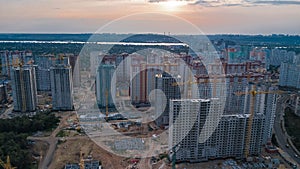 Aerial view of construction site of residential area buildings with cranes at sunset from above, urban skyline