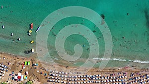 Aerial view of Coral Bay beach with umbrellas, swimming people in transparent sea water. Pegeia, Paphos District, Cyprus
