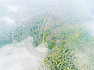 Aerial view of a country road in the forest. Beautiful landscape. Clouds over the green forest and road. Aerial bird`s eye road.