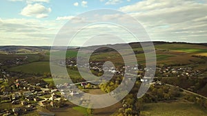 Aerial view of countryside village with small houses among green trees with farm fields and distant forest in summer.