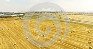 Aerial view of cropped wheat field with bales of hay in the countryside. View of the highway with driving cargo on a