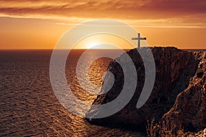 Aerial view of a crucify on the edge of a cliff against the sea and sunset.