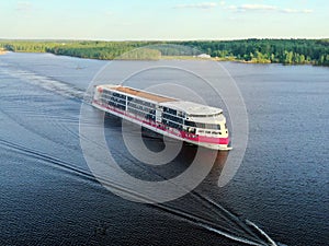 Aerial view cruise ship sails along the river surrounded by a beautiful green forest in the summer at sunset. Cruise Ship