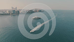 Aerial view of cruising motorboat and unknown anchored luxury motor yacht offshore in Dubai, UAE