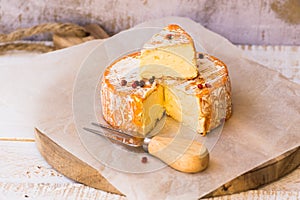 Aerial view of cut slice of French or German soft cheese with orange rind with mold, creamy texture, red pepper corns, waxed paper