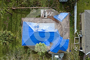 Aerial view of damaged in hurricane Ian house roof covered with blue protective tarp against rain water leaking until