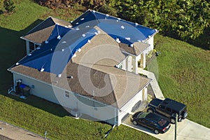 Aerial view of damaged in hurricane Ian house roof covered with blue protective tarp against rain water leaking until