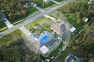 Aerial view of damaged in hurricane Ian house roof covered with blue protective tarp against rain water leaking until