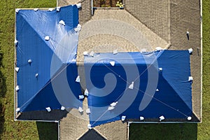 Aerial view of damaged in hurricane Ian house roof covered with blue protective tarp against rain water leaking until