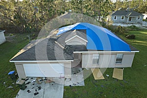 Aerial view of damaged in hurricane Ian house roof covered with blue protective tarp against rain water leaking until photo